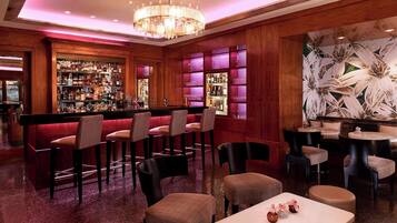 Un área de bar con diversas opciones de asientos, como taburetes y mesas redondas, y una pared decorativa con motivos florales.