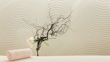 Une serviette soigneusement enroulée, portant en relief l’inscription « LA MER », une branche ornée de fleurs et, en arrière-plan, un mur à texture.