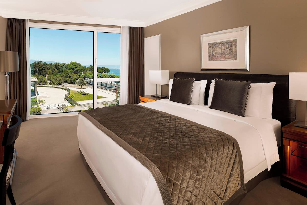 A hotel room with a large bed, a view of a cityscape, and a framed picture on the wall.