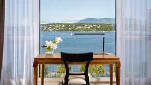 Una mesa de madera con un jarrón de flores blancas, una silla y una vista de un lago con veleros y un pueblo en la ladera.