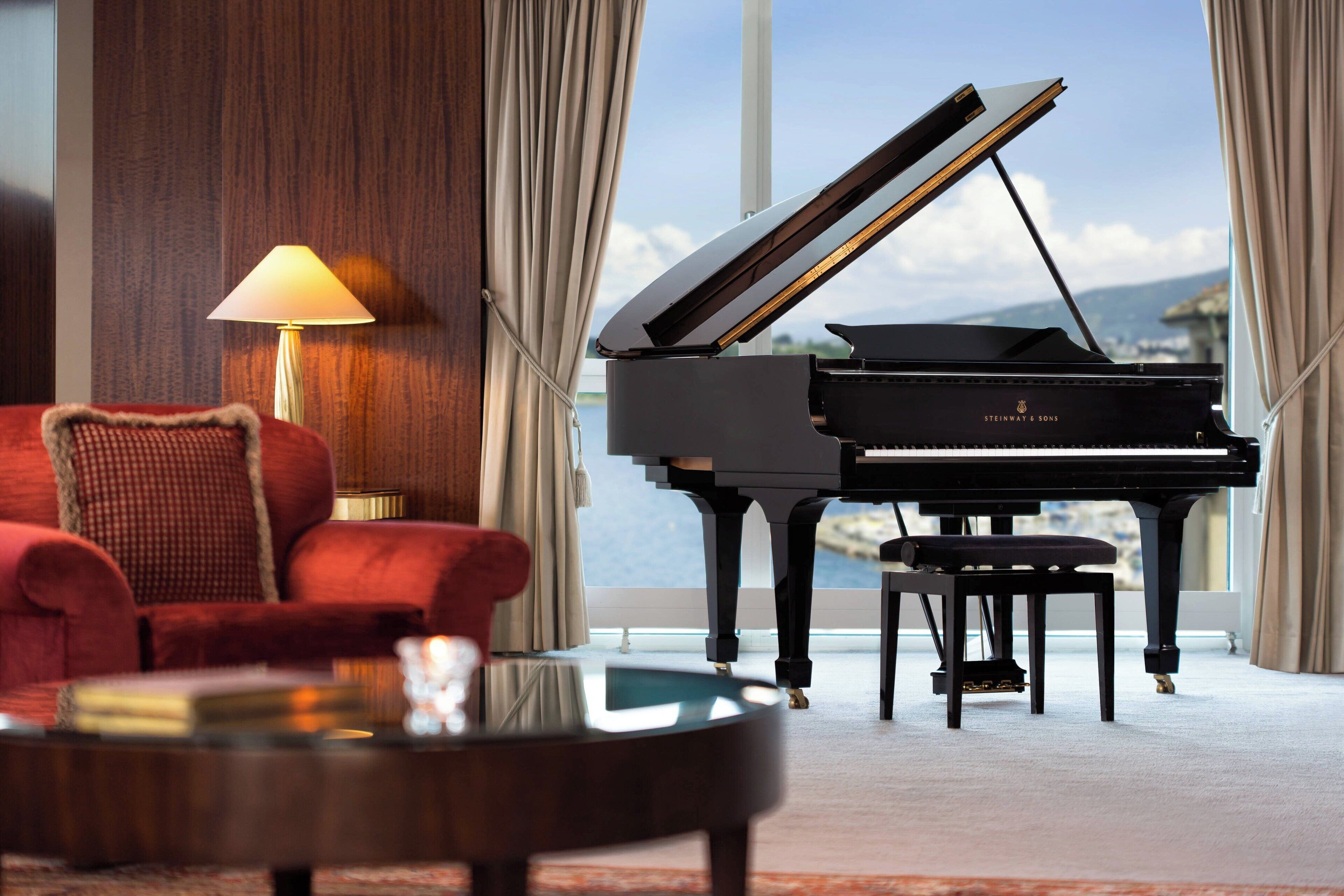 A grand piano in a room with a red sofa and a lamp.