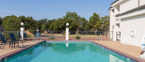 A rectangular swimming pool with clear blue water, surrounded by a brick deck and a metal fence.