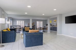 A spacious living area with a dining table and chairs, a kitchen area with a flat-screen TV, and a large window with blinds. - Days Inn by Wyndham Granbury (Granbury)