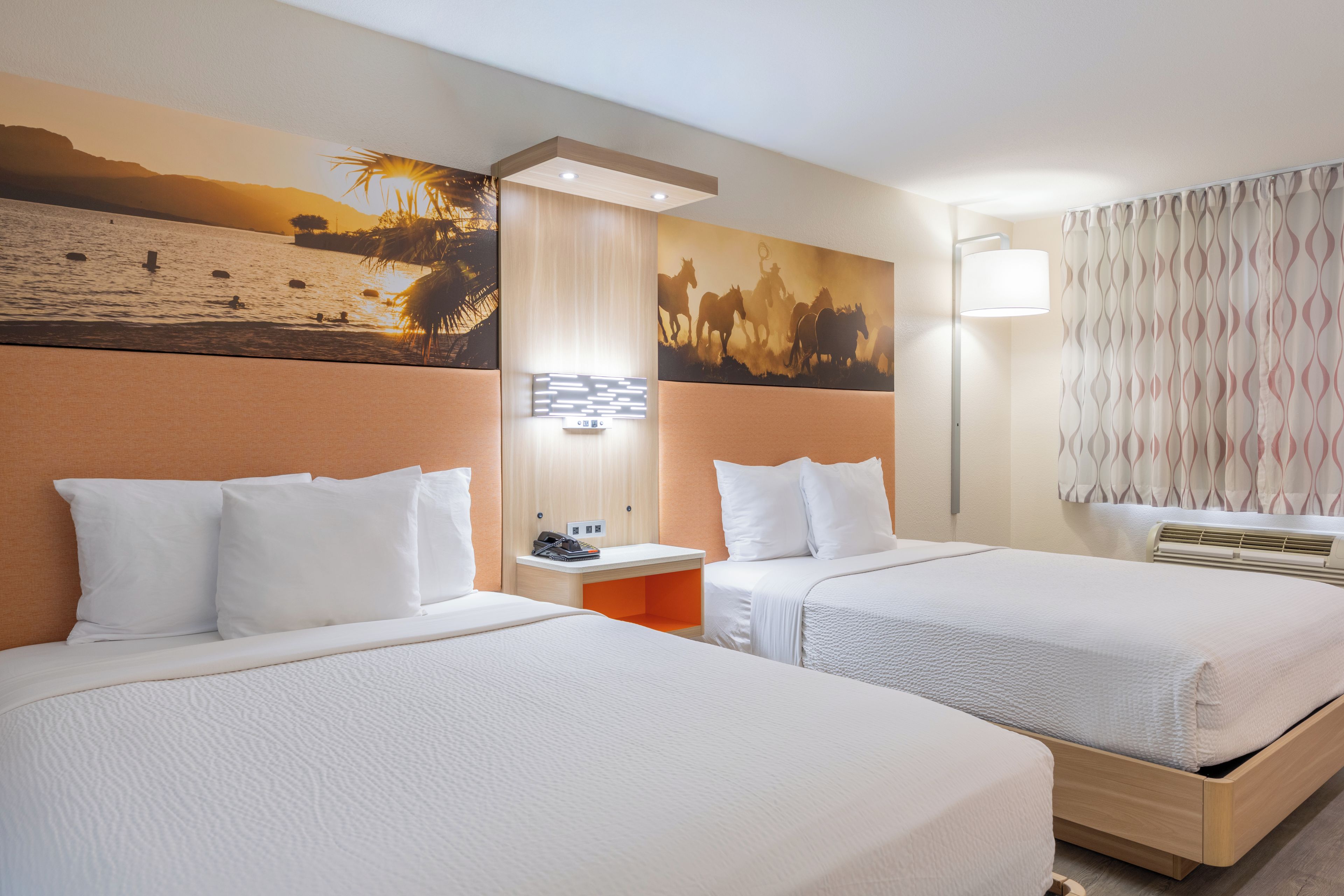 A hotel room with two beds, a nightstand, a telephone, and a wall-mounted light fixture.