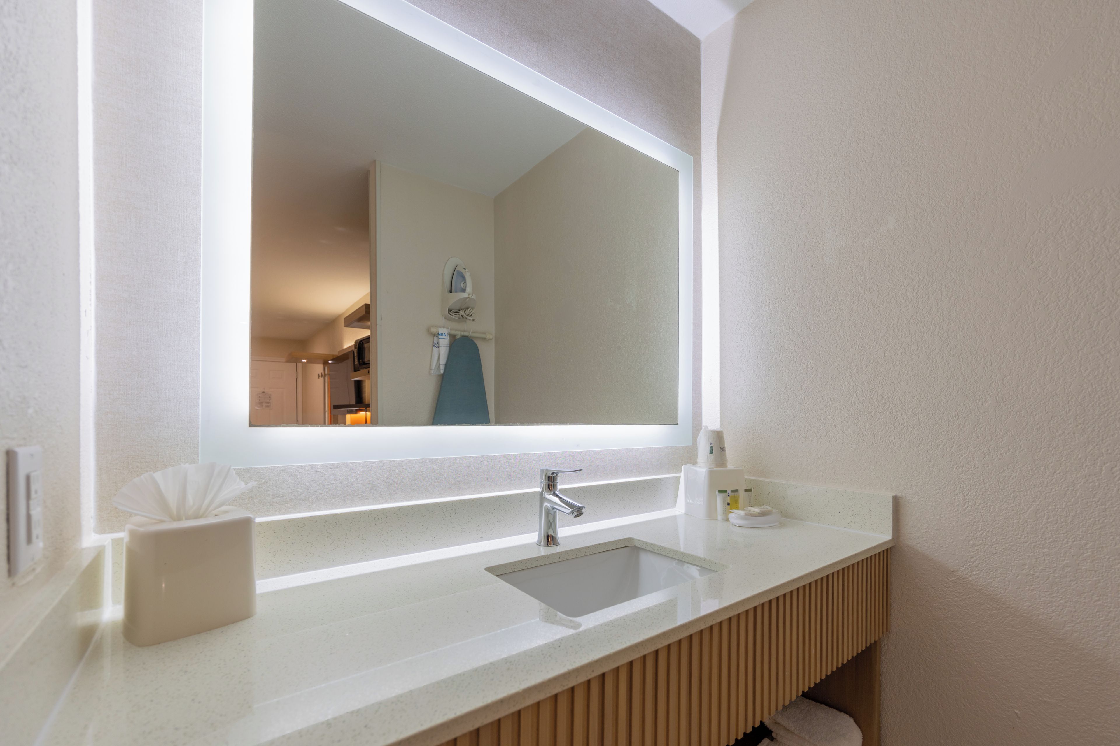 A bathroom with a large mirror, a sink, and a vanity with a towel rack.