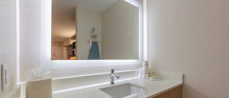 A bathroom with a large mirror, a sink, and a vanity with a towel rack.