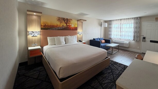 A hotel room with a bed, a desk, a chair, a painting on the wall, and a window with curtains. - Days Inn by Wyndham Granbury (Granbury)