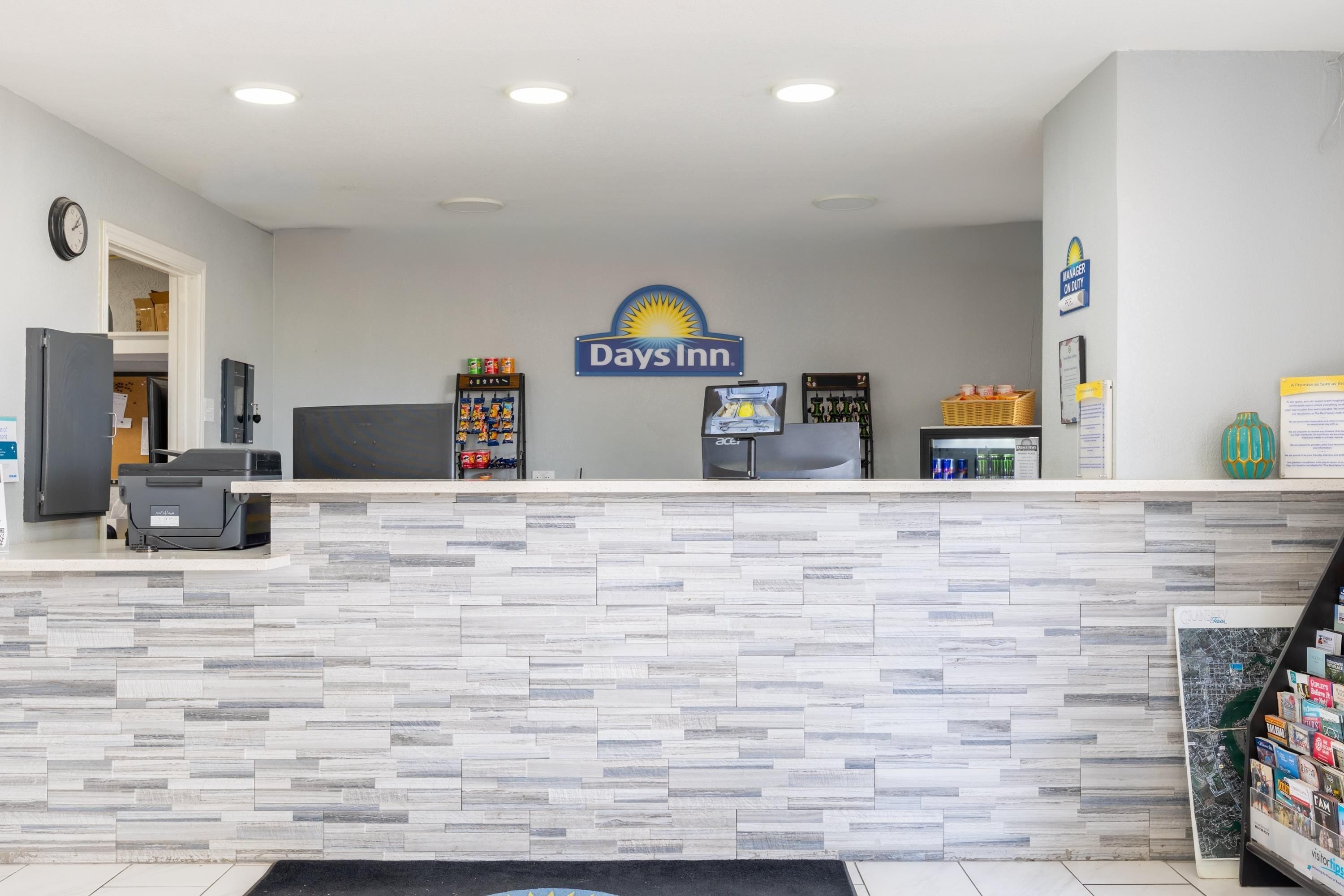 Un área de recepción con el letrero de Days Inn, un reloj, una impresora y una pequeña variedad de aperitivos.