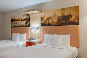 Habitación de hotel con dos camas, una mesita de noche, un teléfono en la pared y un cuadro de caballos.