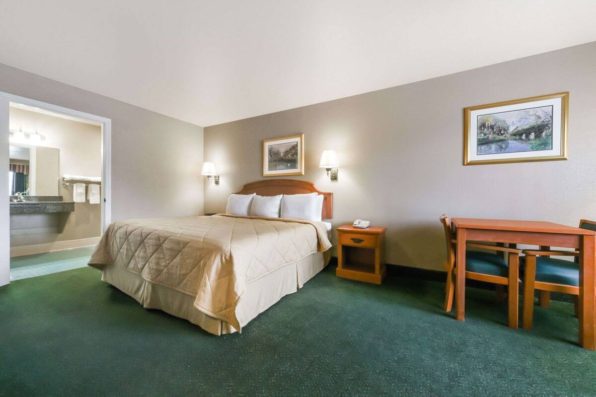 Ein Hotelzimmer mit Bett, Nachttisch, Lampe, Stuhl und einem Bild an der Wand.