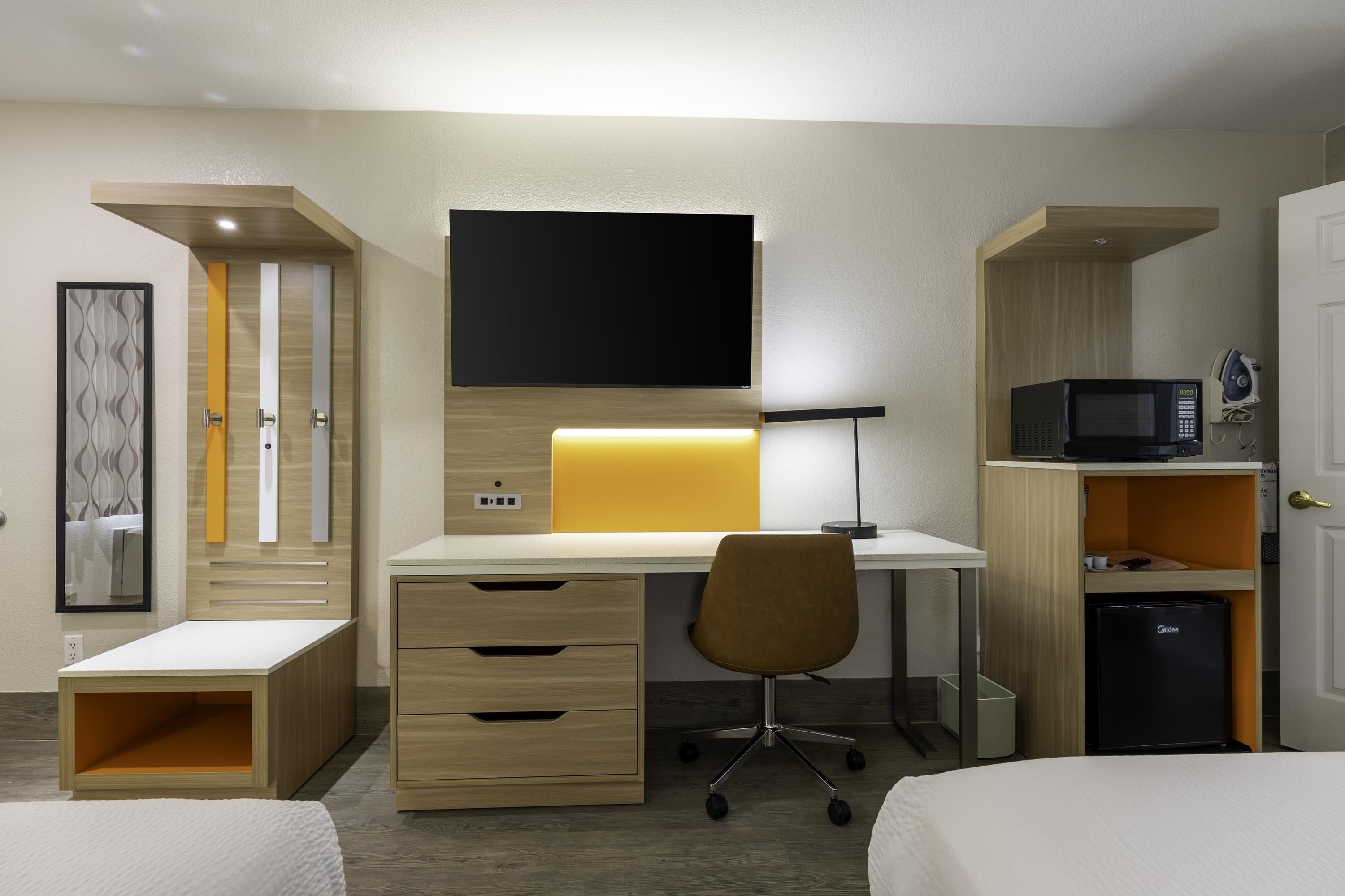 Een hotelkamer met een bed, een bureau met een computer, een stoel, een magnetron en een kleine koelkast.