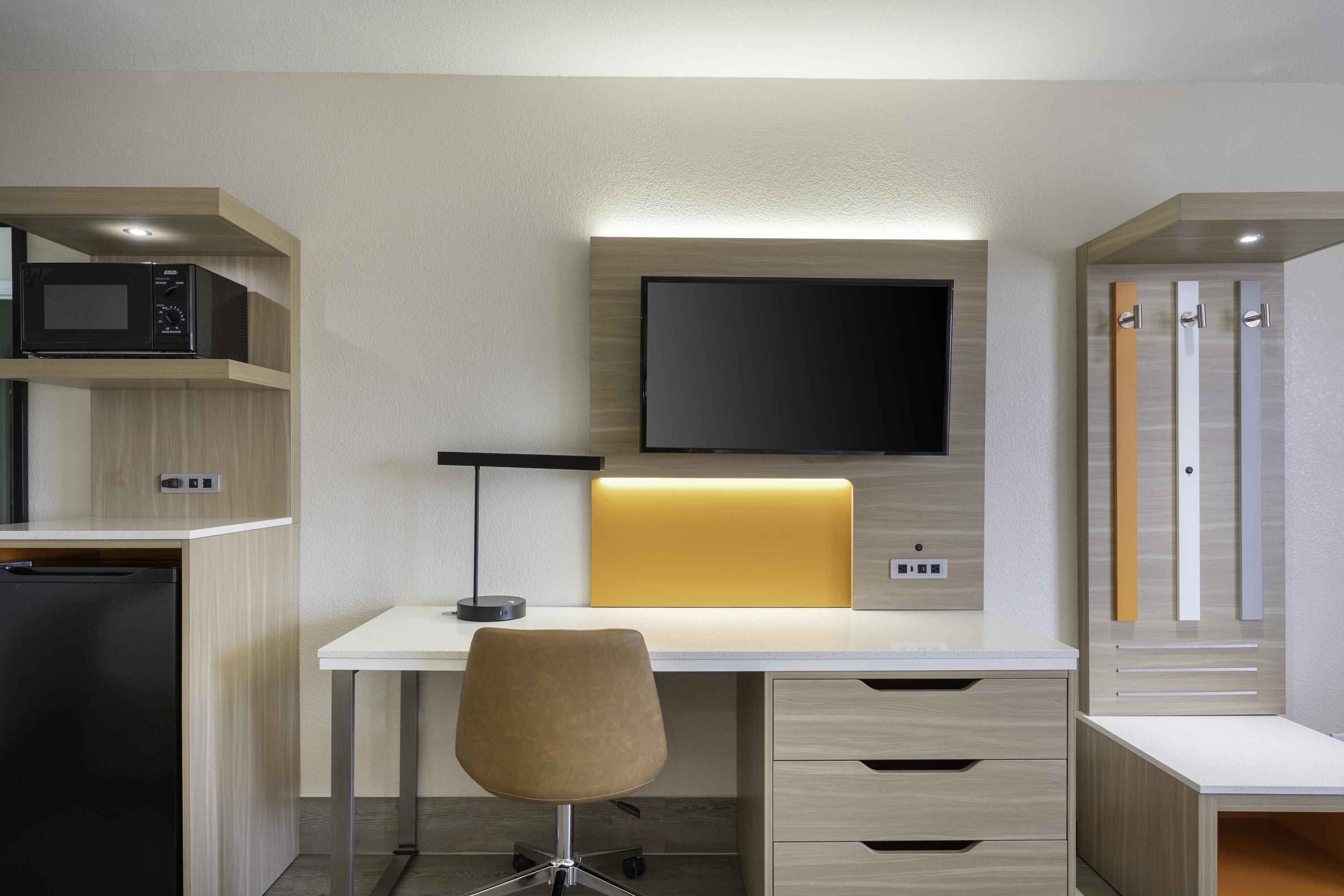 Een moderne, goed verlichte kantoorruimte met een bureau, stoel, ingebouwde magnetron en een flatscreen televisie.