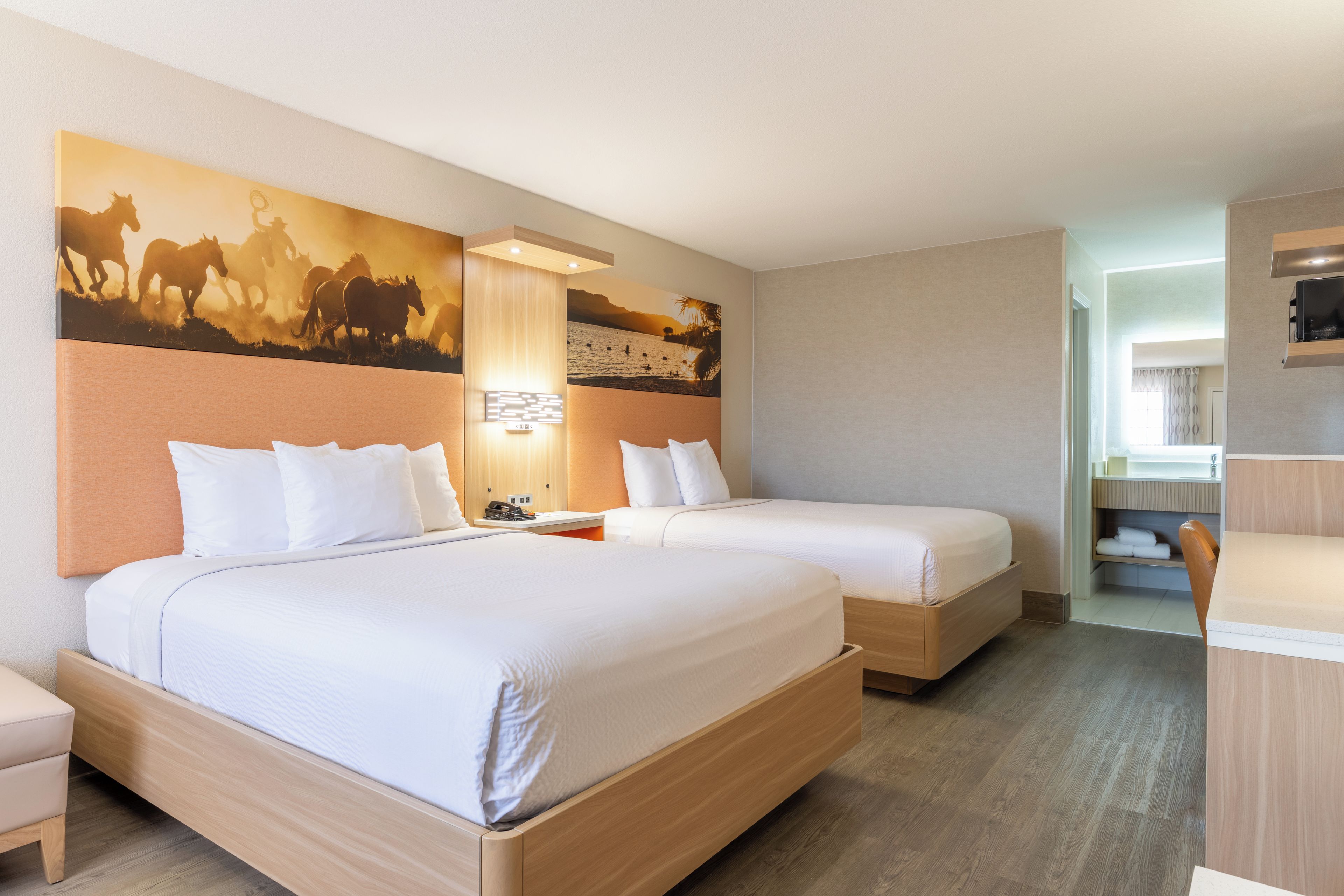 A hotel room with two beds, a large wall mural, a desk, and a bathroom visible through an open door.
