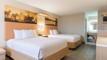 A hotel room with two beds, a large wall mural, a desk, and a bathroom visible through an open door.