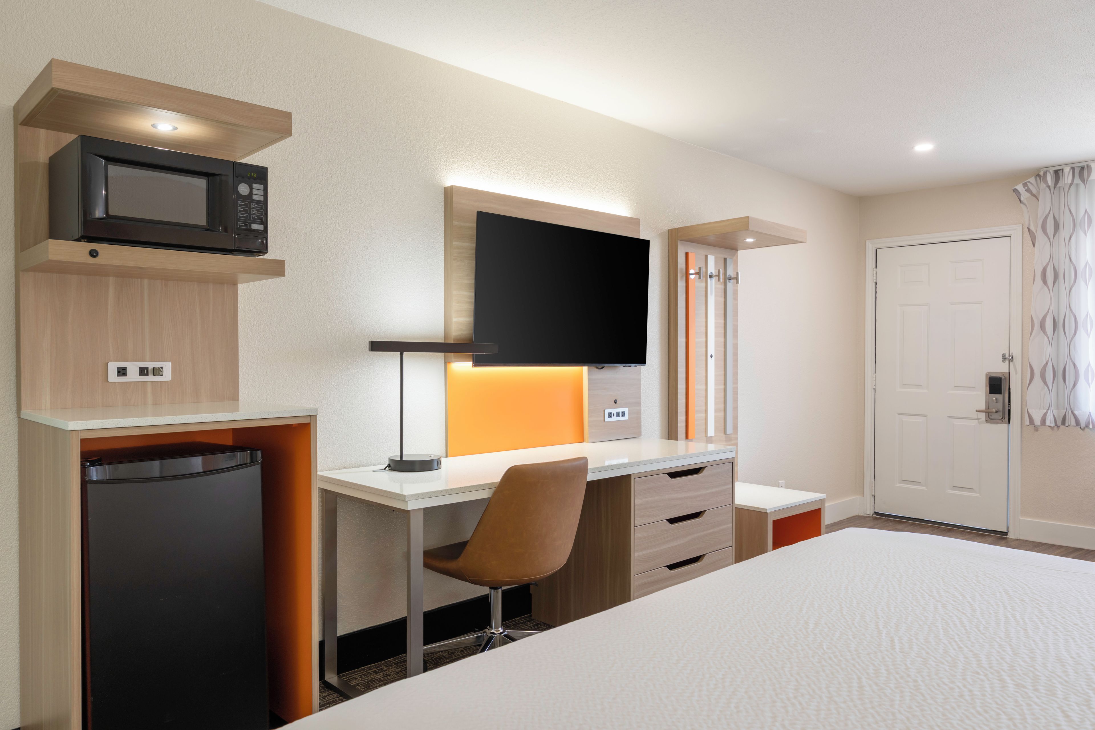 A hotel room with a bed, a desk with a computer, a microwave, and a television.
