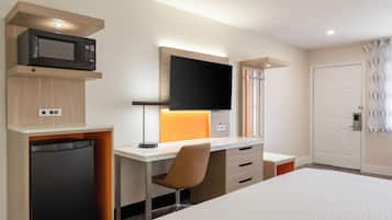 A hotel room with a bed, a desk with a computer, a microwave, and a television.