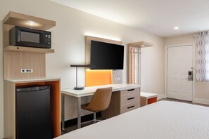 A hotel room with a bed, a desk with a computer, a microwave, and a television.