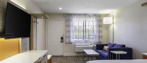 Habitación de hotel con cama, escritorio, silla, televisor, ventana con cortinas y lámpara.