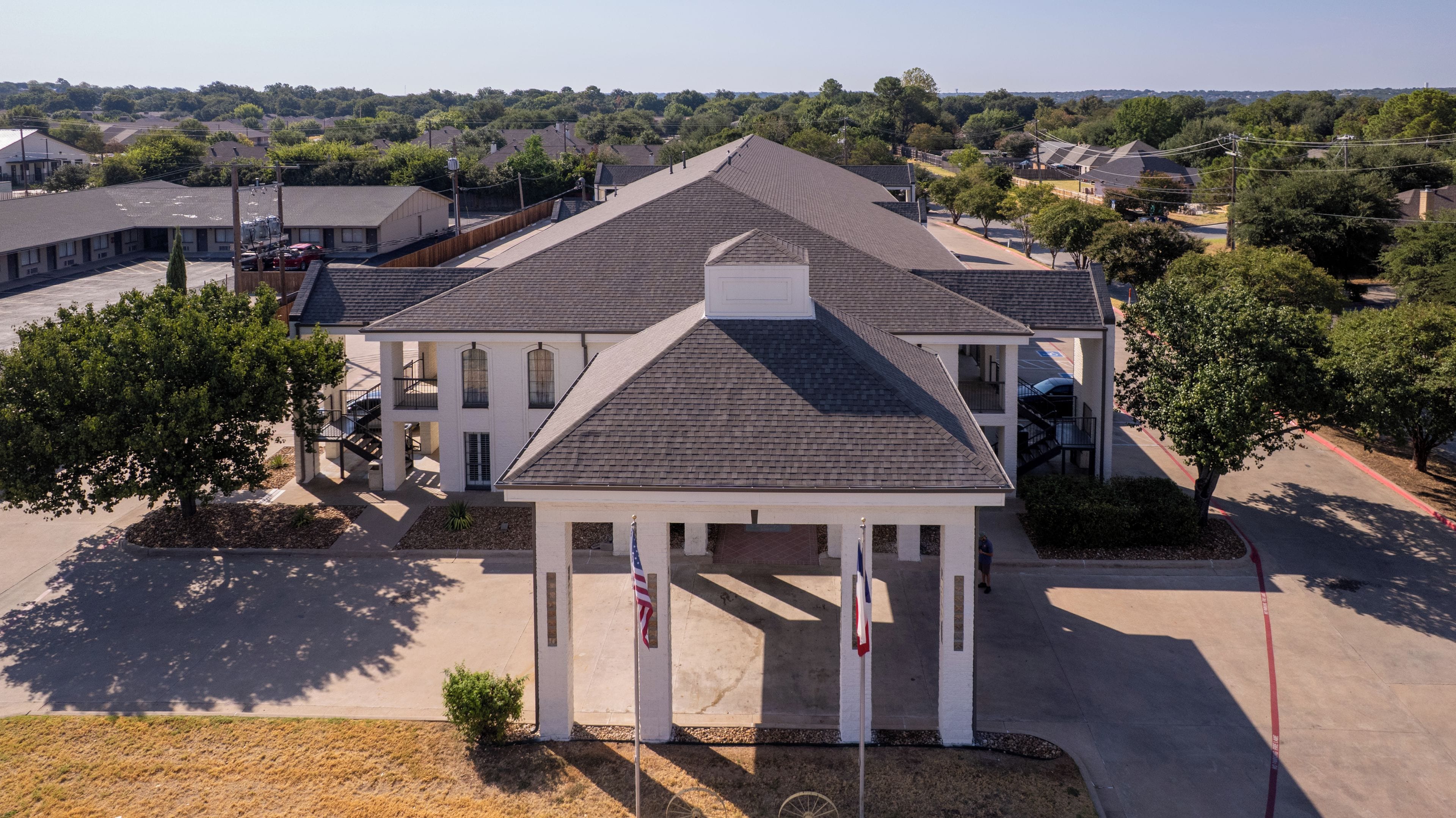 A two-story building with a central courtyard, flagpoles, and a parking lot.