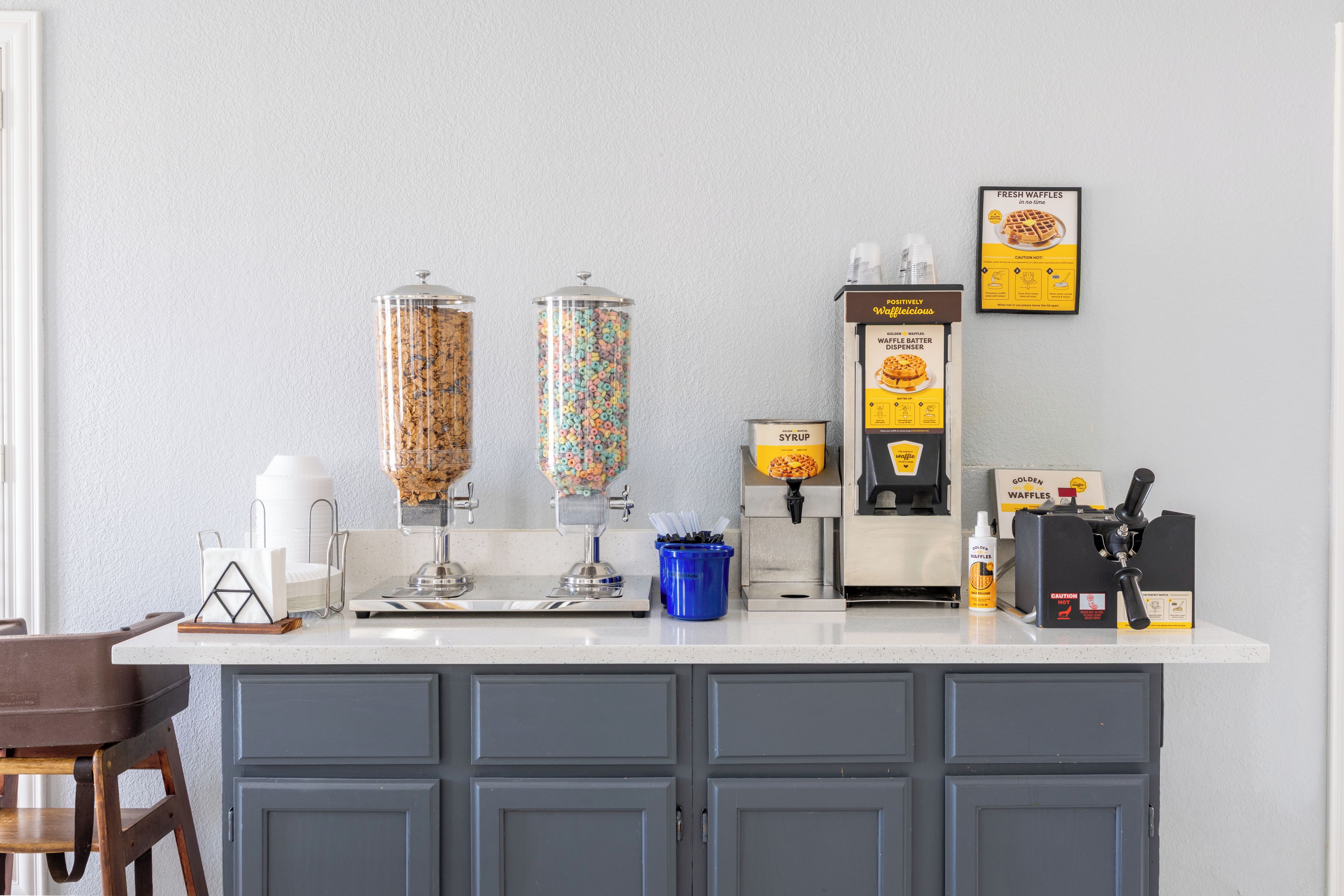 A kitchen counter with waffle dispensers, syrup, and waffle batter dispenser.