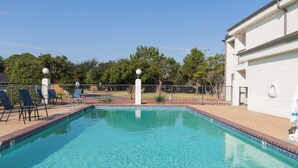 A clear swimming pool with a tiled edge, surrounded by a fence, and a building with a white exterior in the background. - Days Inn by Wyndham Granbury (Granbury)