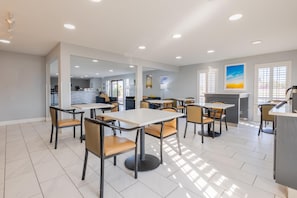 A modern dining area with multiple tables and chairs, a kitchen in the background, and large windows allowing natural light. - Days Inn by Wyndham Granbury (Granbury)