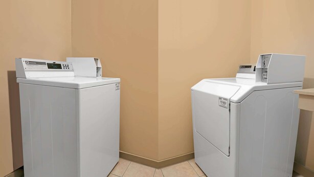 Two white front-loading washing machines in a corner of a room with beige walls and tiled flooring. - Days Inn by Wyndham Granbury (Granbury)