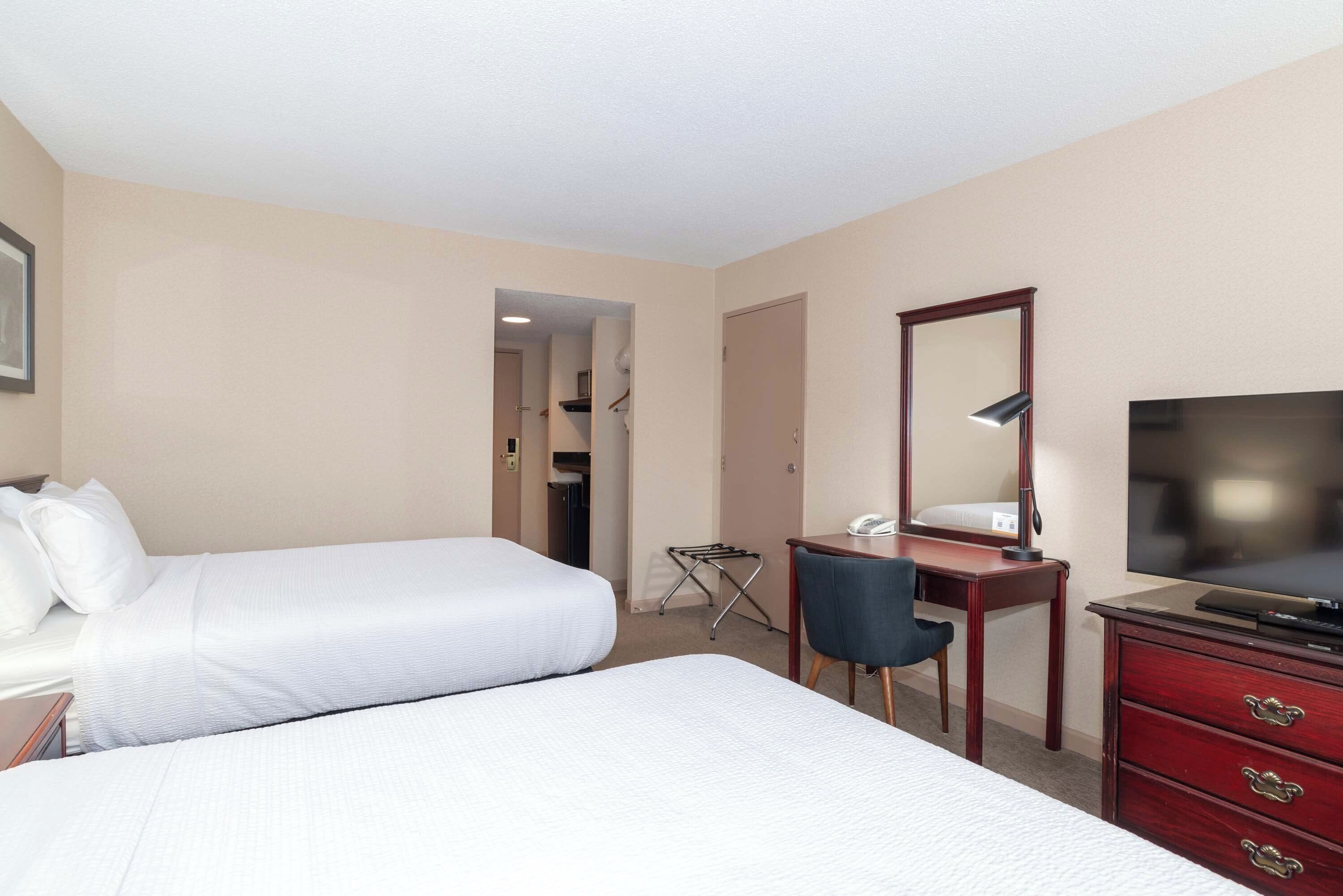 Habitación de hotel con dos camas, un escritorio, una silla, un televisor y un aparador.