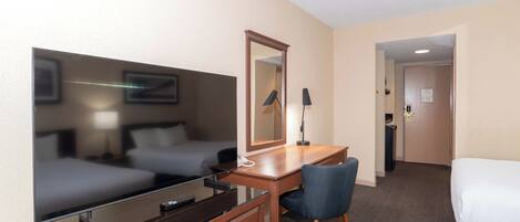 Una habitación de hotel con cama, escritorio, silla, televisor y espejo.