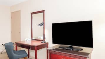 Una camera d'albergo con una scrivania in legno, una sedia, una televisione e un comò.