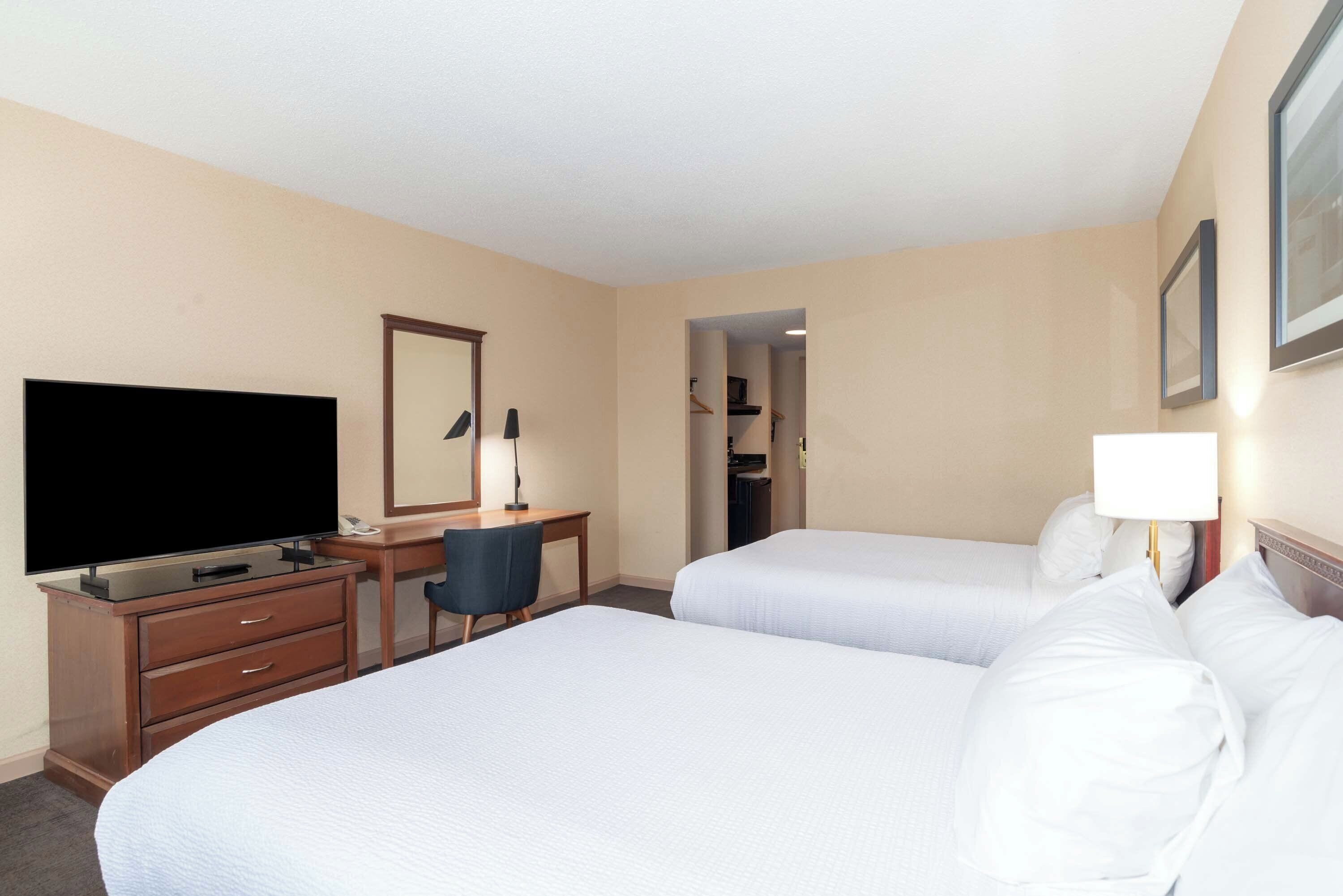 A hotel room with two beds, a desk with a chair, a television, and a mirror.