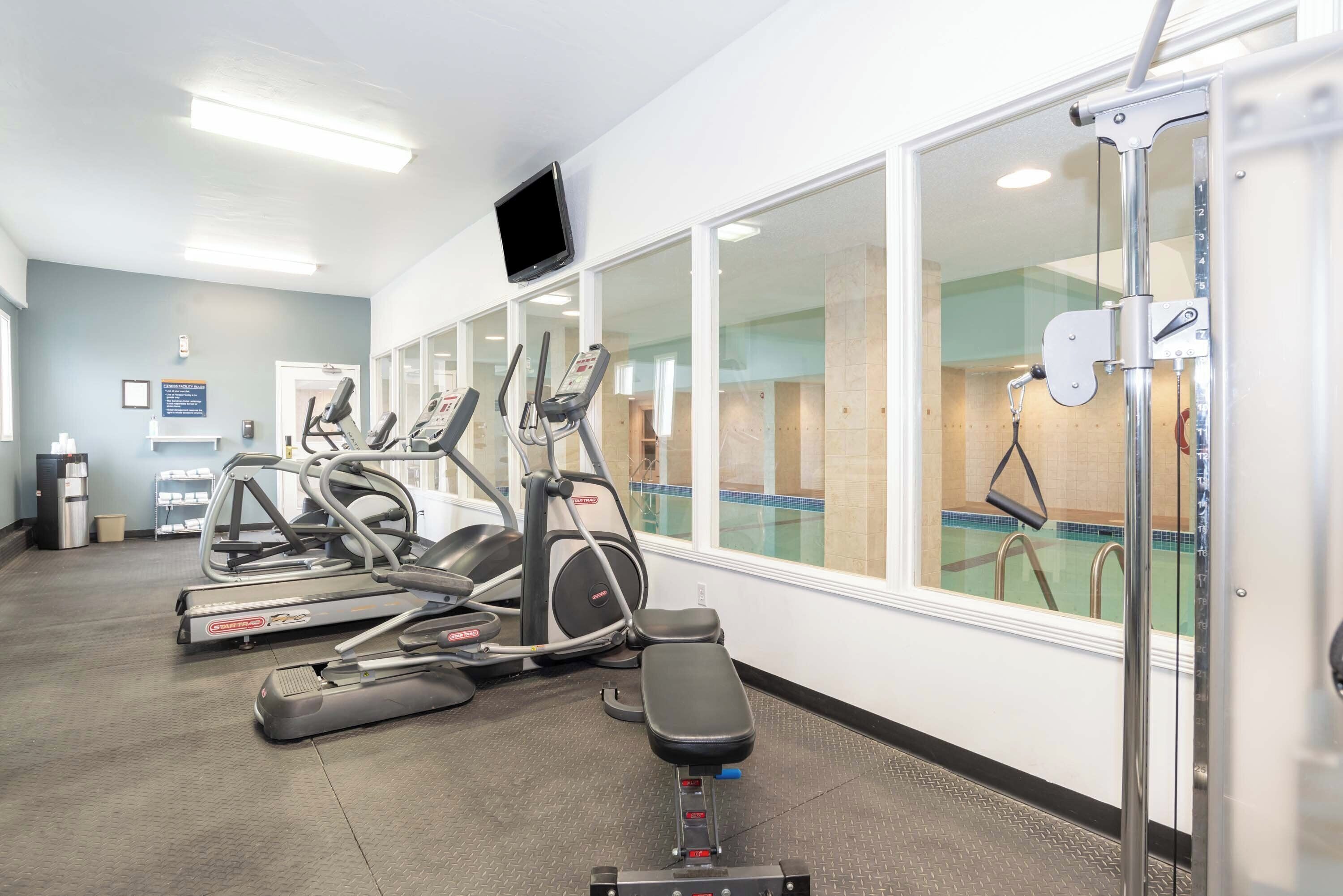 A gym with treadmills, elliptical machines, and a bench.