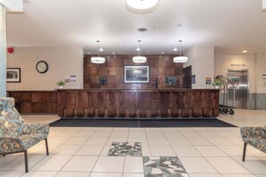 A reception area with a wooden counter, two pendant lights, a clock, and a framed picture on the wall. - Sandman Hotel Lethbridge (Lethbridge)