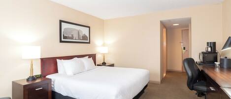 Una habitación de hotel con una cama grande, dos mesitas de noche con lámparas, un escritorio con una silla y un cuadro enmarcado en la pared.