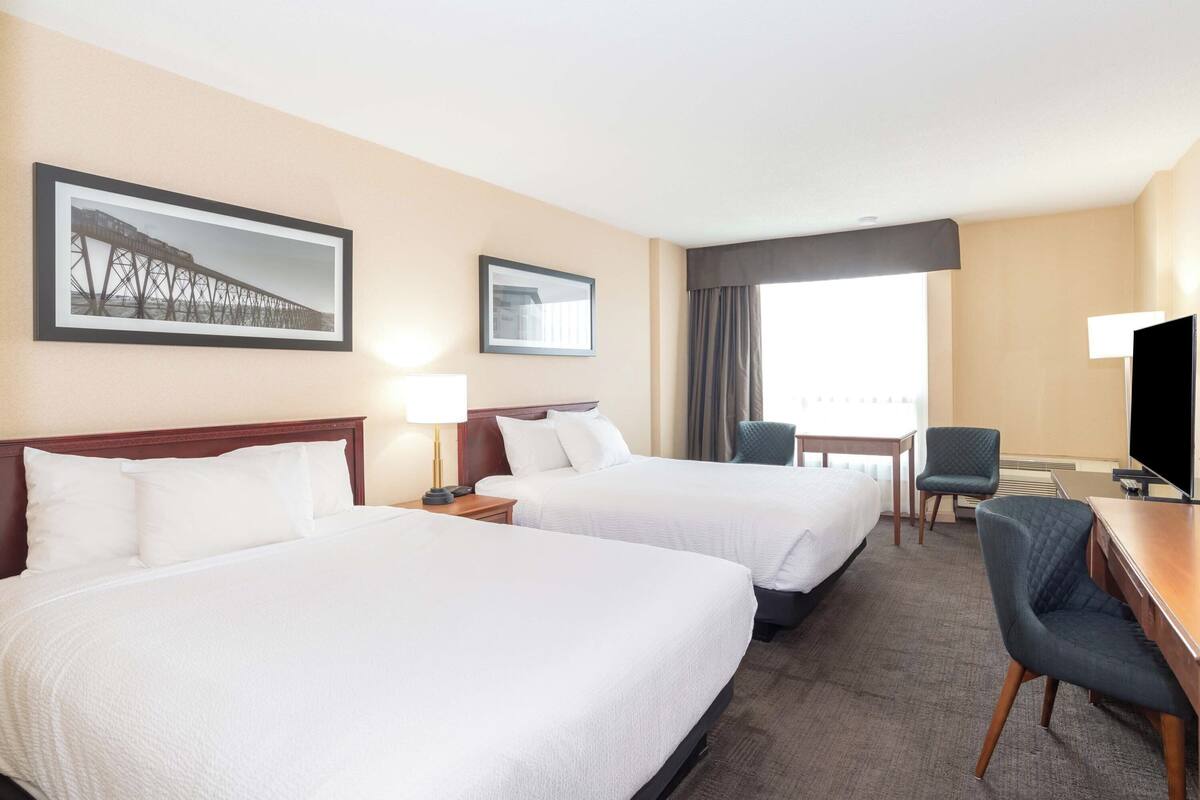 A hotel room with two beds, a desk, a chair, a TV, and a window with curtains.