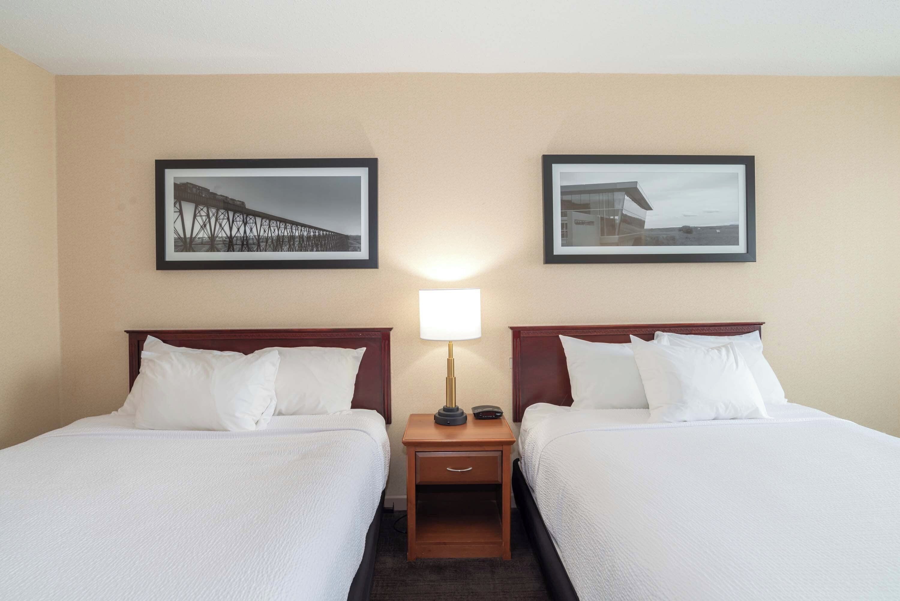 Une chambre d’hôtel avec deux lits, une table de chevet avec une lampe et deux tableaux encadrés au mur.