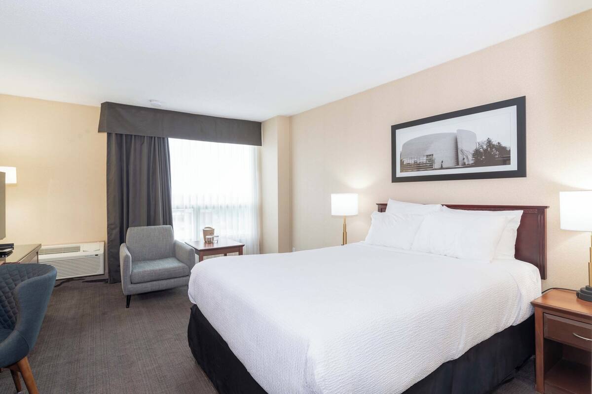 A hotel room with a large bed, a desk, a chair, and a window with curtains.