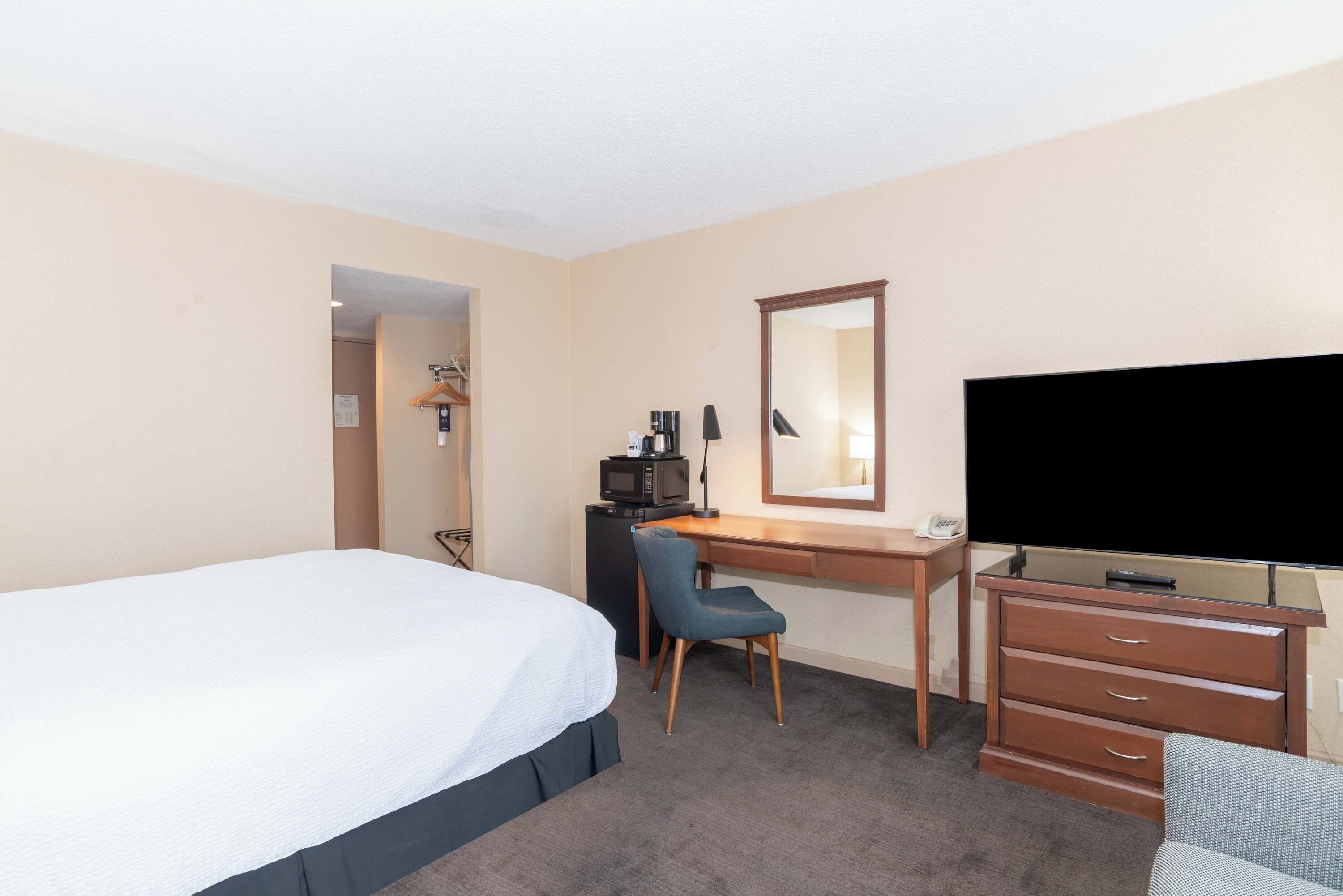 Une chambre d’hôtel équipée d’un lit, d’un bureau avec une chaise, d’une télévision, d’une commode et d’un four à micro-ondes.