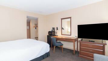 Une chambre d’hôtel équipée d’un lit, d’un bureau avec une chaise, d’une télévision, d’une commode et d’un four à micro-ondes.
