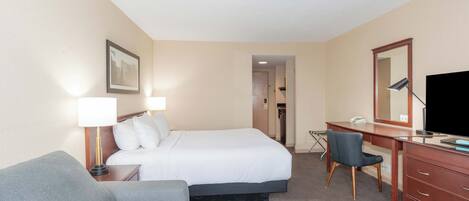 Una habitación de hotel con cama, escritorio, silla, televisor y lámpara.