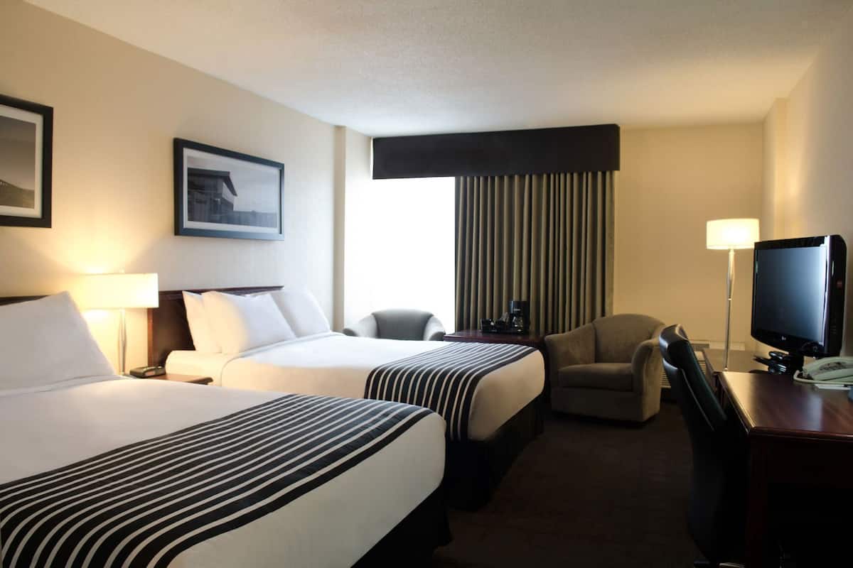 A hotel room with two beds, a desk with a computer, a chair, a lamp, and a television.