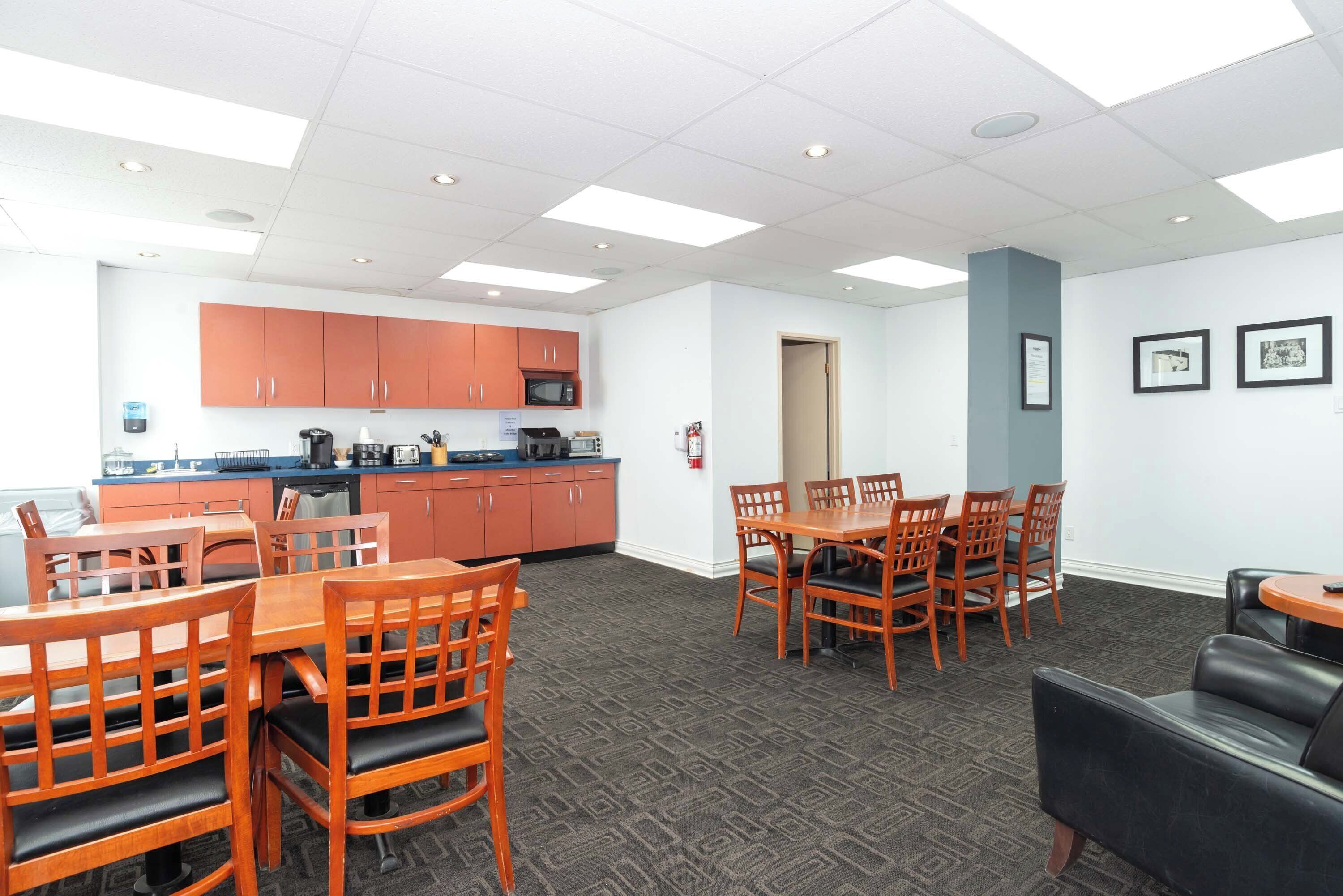 A dining area with wooden tables and chairs, a kitchen with orange cabinets, and framed pictures on the wall.