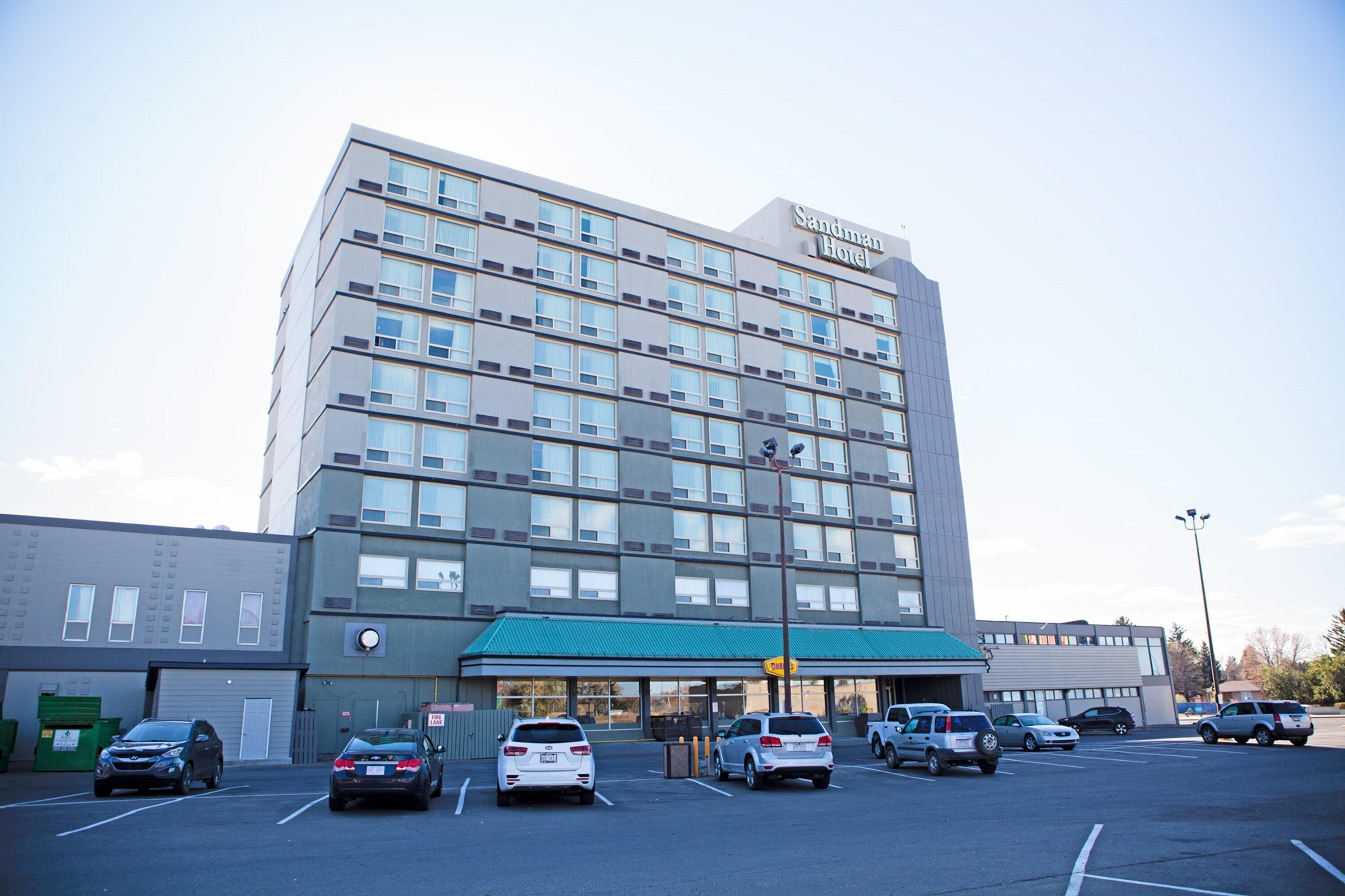 A multi-story hotel with a flat facade, a green awning, and a parking lot with several cars.