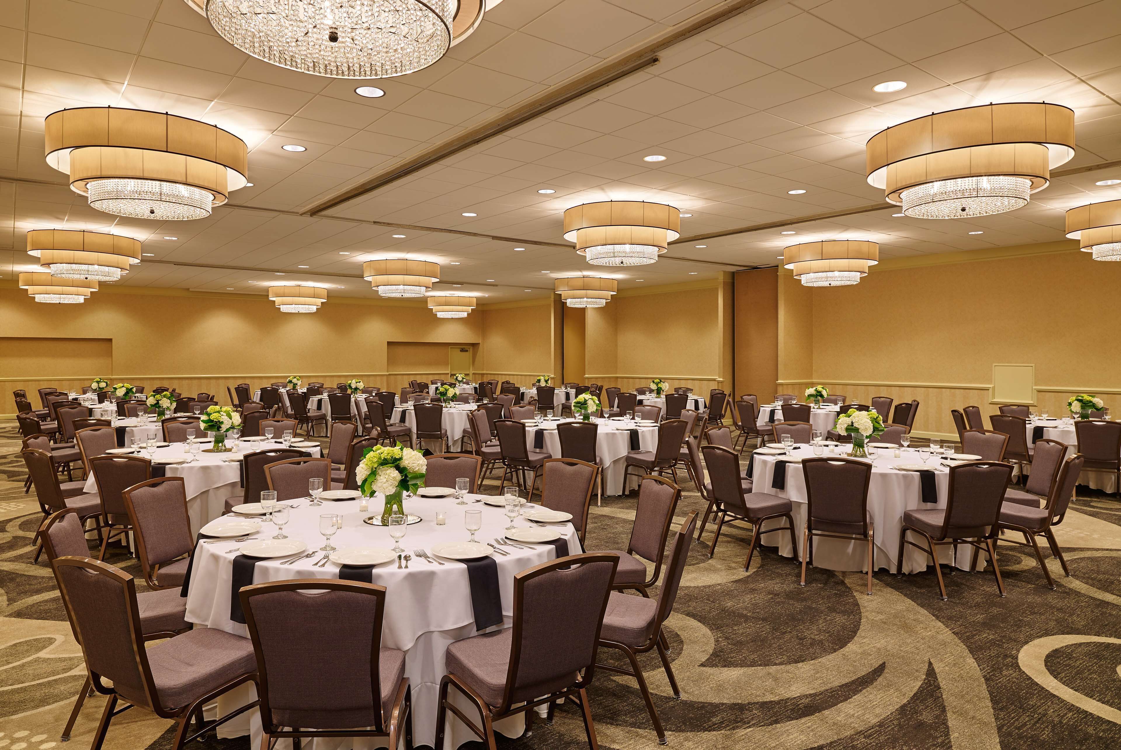 A banquet hall with round tables, chairs, and chandeliers.