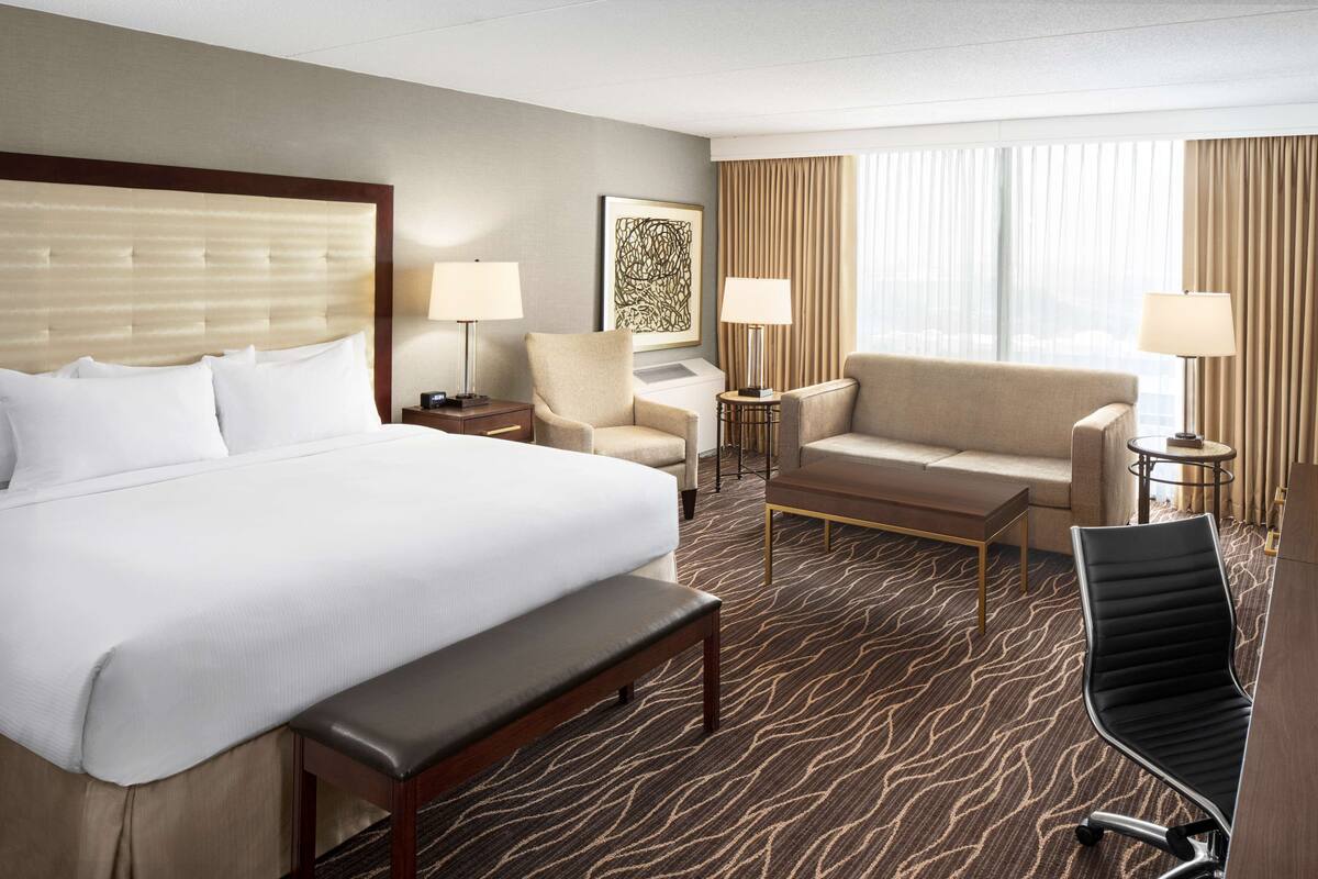 Habitación de hotel con una cama grande, un banco, un sofá, una silla y un escritorio con lámparas.