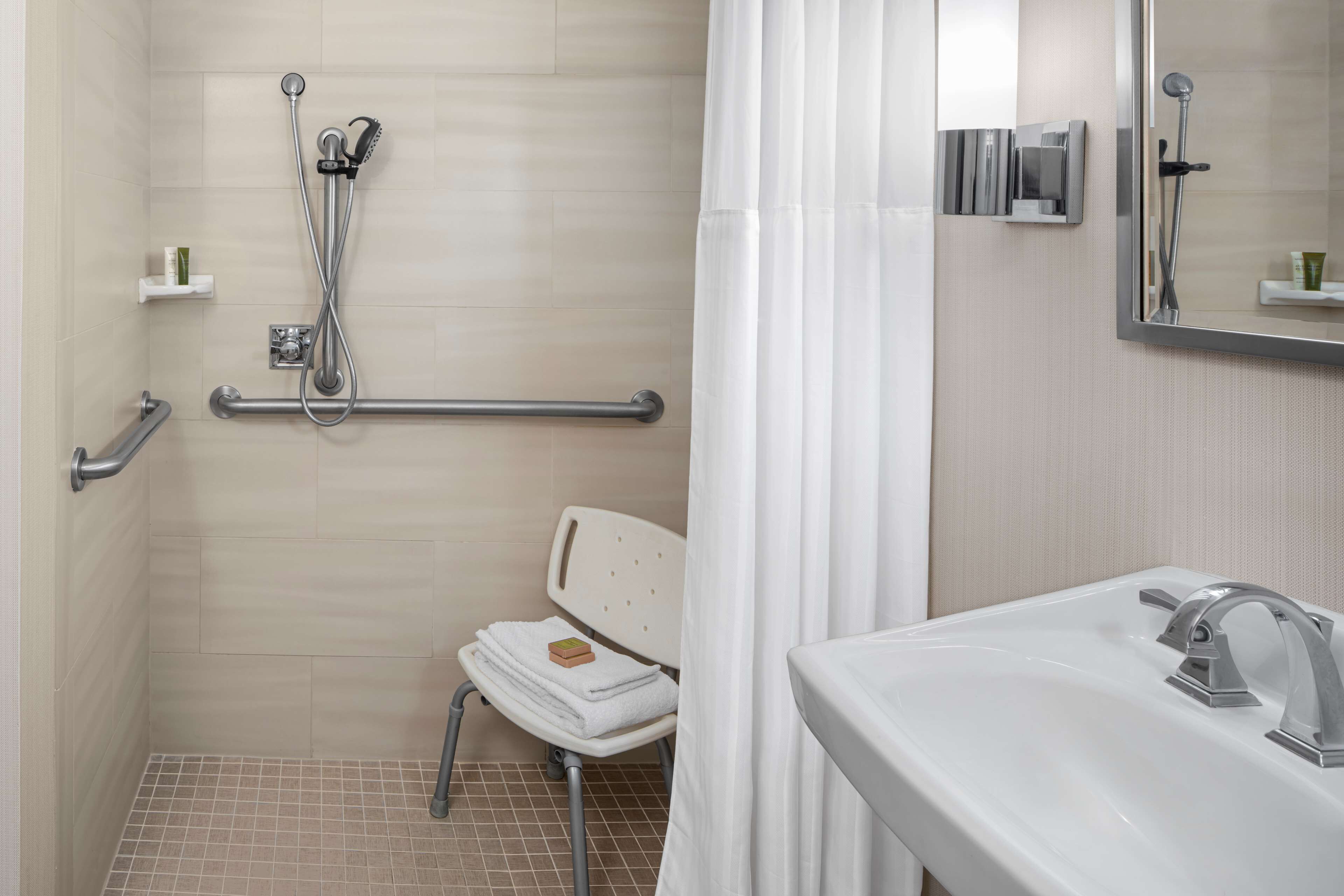 A bathroom with a shower, grab bars, a white sink, and a mirror.
