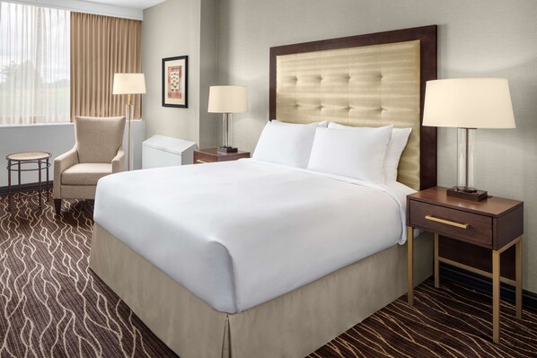 A hotel room with a large bed, two bedside tables with lamps, a chair, and a patterned carpet.