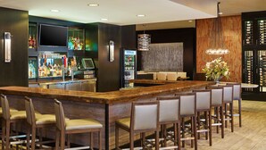 A bar area with a long wooden counter, multiple bar stools, a minibar, and a large wine rack. - Hilton Kansas City Airport (Kansas City)