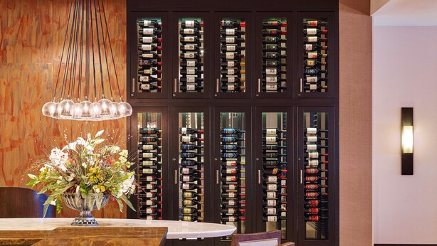 A dining area with a wooden table, chairs, a vase of flowers, and a wine rack with bottles. - Hilton Kansas City Airport (Kansas City)