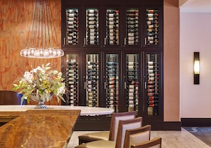 A dining area with a wooden table, chairs, a vase of flowers, and a wine rack with bottles.